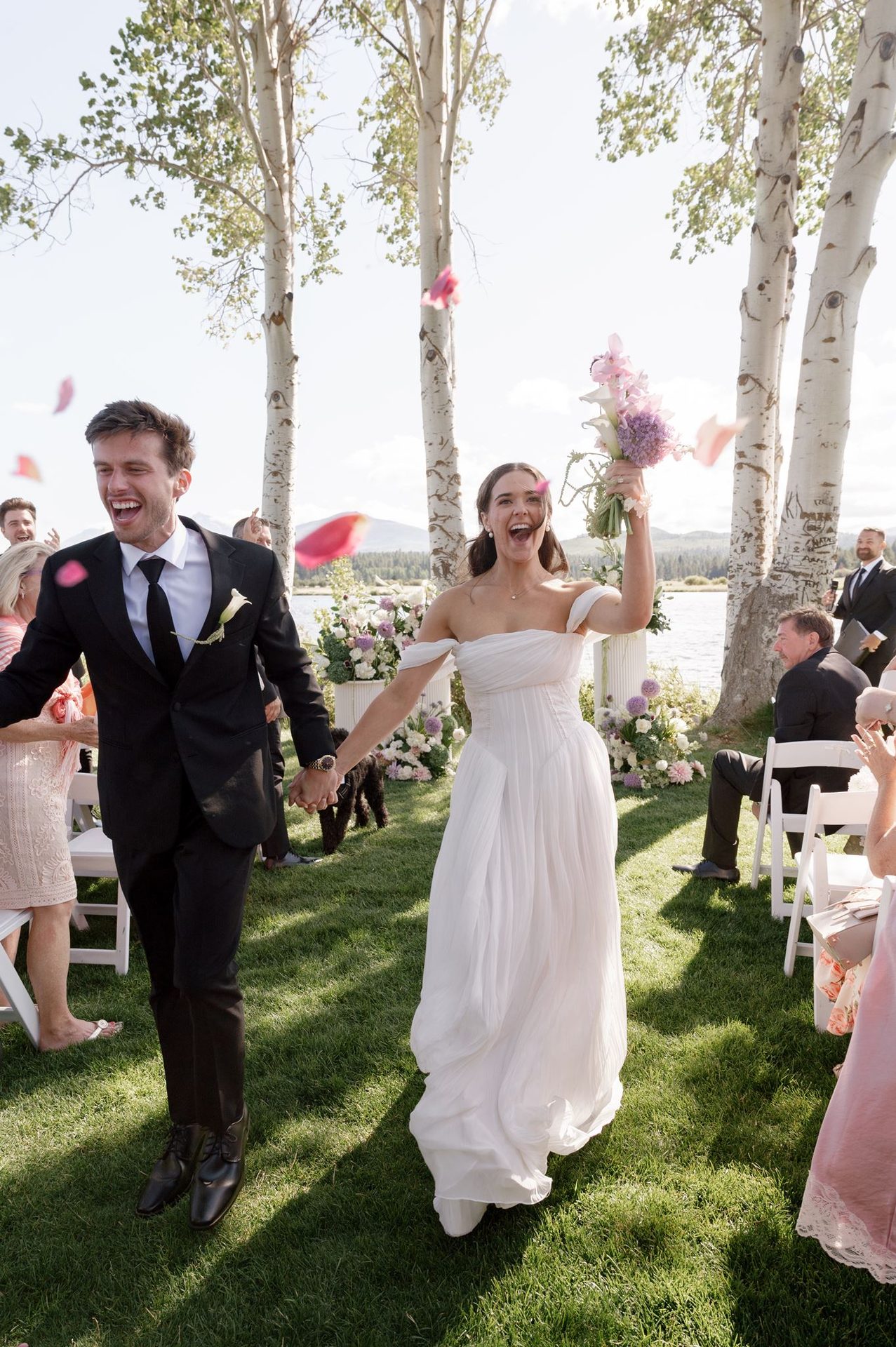 Just-married recessional by the water, petals in the air